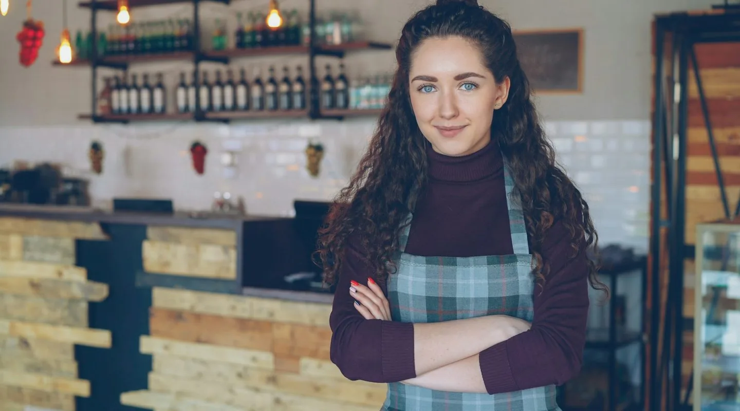 Dona de café sorrindo de braços cruzados no balcão