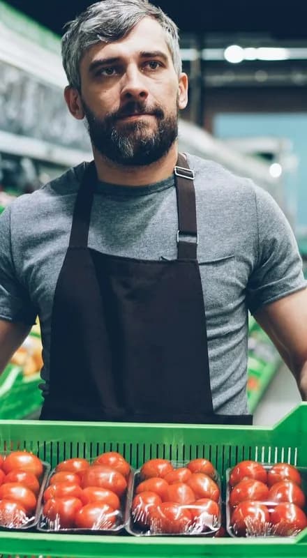 Funcionário de mercado segurando uma caixa de tomates